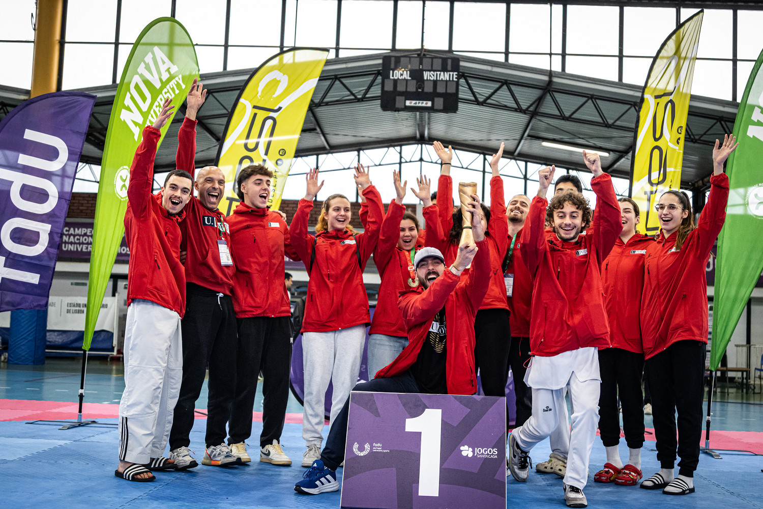 12 estudantes atletas de taekwondo vencedores do troféu coletivo no cnu. todos de casaco vermelho da universidade, com o treinador cláudio varejão.